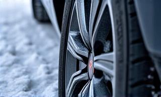 Ein Detailbild eines Winterreifens mit einem Schneeflockensymbol, liegt auf einer leicht vereisten Fahrbahn.